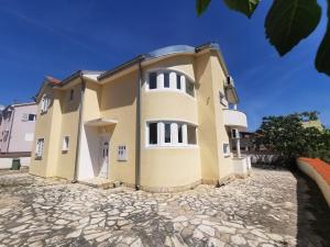 a large yellow building on a stone driveway at Apartmani Lešić Tribunj in Tribunj