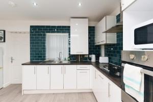 una cocina con armarios blancos y una pared de azulejos verdes en Fewston House, en Leeds