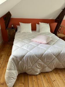 uma cama com um edredão branco e uma almofada rosa em Gîte des Tourterelles em Épineuil-le-Fleuriel