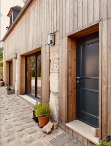 un edificio de madera con una puerta negra y algunas plantas en La Cour Verte : Chaleureuse grange réhabilitée, en Montépilloy