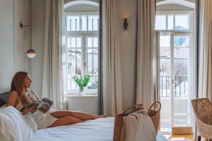 une femme assise sur un lit en train de lire un livre dans l'établissement Allegro Neve Tzedek Boutique Suites - By HOMY, à Tel Aviv