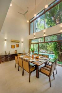 a dining room with a table and chairs and large windows at SaffronStays Miraya - Nature Retreat, Pool, Games, Bar in Alibaug in Alibaug