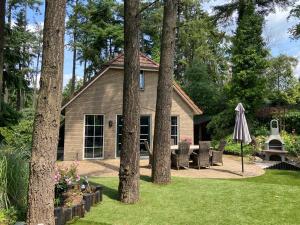 a house with a yard with chairs and an umbrella at Wellness Bosboerderij de Goudsberg met hottub en sauna in Lunteren