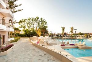 a resort pool with lounge chairs and umbrellas at Porto Platanias Village Resort in Plataniás