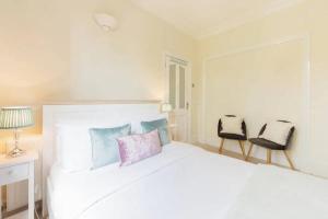 a white bedroom with a white bed and two chairs at Charming 3BD Flat - 5 Minutes to Victoria Park in London