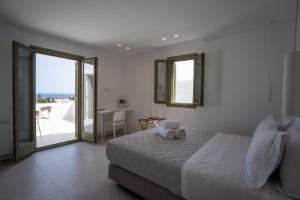 Paros Breeze Luxury Villa في دريوس: غرفة نوم بيضاء مع سرير وشرفة
