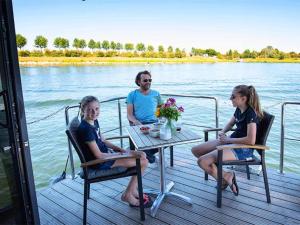 3 Personen sitzen an einem Tisch auf einem Boot auf dem Wasser in der Unterkunft Lovely houseboat in Kinrooi with terrace in Kinrooi