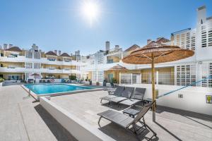 a patio with chairs and an umbrella and a swimming pool at Delightful Cabanas 2 Bedroom apartment in Cabanas de Tavira