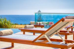 a row of wooden tables sitting next to the ocean at Villa Kore Luxuryvillaschania in Falasarna