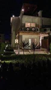 una casa de noche con palmeras delante en فيلا مميزه جدا في الساحل الشمالي ستيلا هايتس Stella Heights - Sidi Abd El-Rahman villa type M, en El Alamein