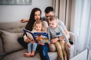 Una famiglia seduta su un divano a leggere un libro di Rezydencja Park Mielno a Mielno