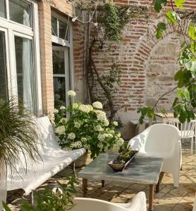 een patio met 2 witte stoelen, een tafel en bloemen bij La maison sur la place in Penne-dʼAgenais