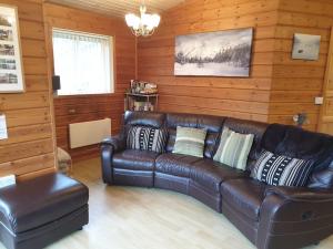 un sofá de cuero marrón en una habitación con paredes de madera en Luxury Peak District lodge, hot tub, log burner, nr lake en Rudyard