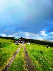 a barn in a field with a rainbow in the sky at Horská bouda KUPROVKA in Strážné