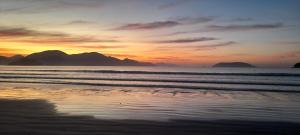 - un coucher de soleil sur une plage avec des montagnes en arrière-plan dans l'établissement Sacada gourmet, piscina e ar condicionado, à Ubatuba