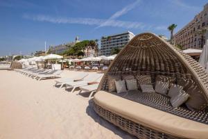 - un lit en osier sur une plage avec des chaises et des parasols dans l'établissement Palais Miramar - Suite White Jardin - 20m Plage, à Cannes