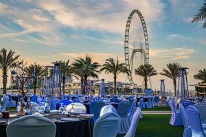 een groep tafels en stoelen met een reuzenrad op de achtergrond bij DoubleTree by Hilton Dubai Jumeirah Beach in Dubai