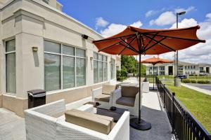 une terrasse avec des chaises blanches et un parasol dans l'établissement Hilton Garden Inn Gulfport - Biloxi Airport, à Gulfport