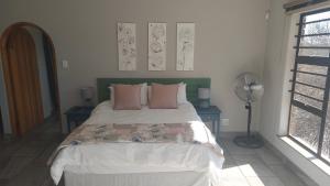a bedroom with a bed with pink pillows and a fan at Skylight Guest House in Harrismith