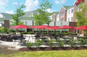 un patio con mesas y sillas y sombrillas rojas en Hilton Garden Inn Milwaukee Northwest Conference Center, en Milwaukee