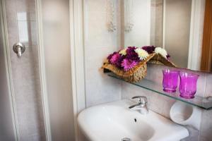 un lavandino in bagno con due bicchieri e fiori su una mensola di Hotel Daniela a Rimini