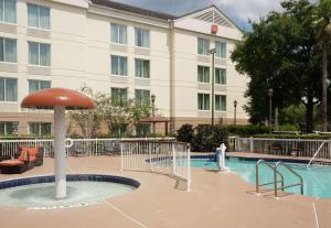 a hotel swimming pool with an umbrella in front of a building at Hilton Garden Inn Orlando Airport in Orlando