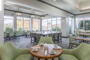 Hilton Garden Inn Tulsa South في تولسا: غرفة طعام مع طاولات وكراسي ونوافذ
