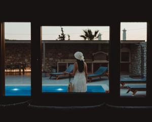une femme en robe blanche qui regarde par une fenêtre dans l'établissement SandShine Luxury Villa, à Kalamaki