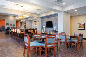 Hampton Inn Kalamazoo في كالامازو: غرفة طعام مع طاولات وكراسي ومدفأة