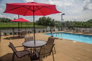 Hampton Inn Summersville في سمرسفيل: طاولة وكراسي مع مظلة حمراء بجوار حمام سباحة
