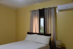 1 dormitorio con 1 cama y una ventana con cortinas blancas en Treasures Gated Community Spot, en Spanish Town