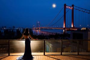 a woman standing on a balcony looking at a bridge at Hilton Wuhan Yangtze Riverside in Wuhan
