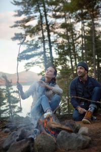 Un uomo e una donna seduti intorno a un fuoco da campo di Hotel Saranac, Curio Collection By Hilton a Saranac Lake