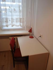 einen weißen Schreibtisch mit einer roten Lampe und einem Fenster in der Unterkunft M2 Art in Giżycko