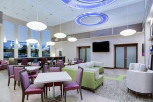 Hampton Inn and Suites Jacksonville/Orange Park, FL في أورانج بارك: غرفة انتظار مع طاولات وكراسي وتلفزيون بشاشة مسطحة