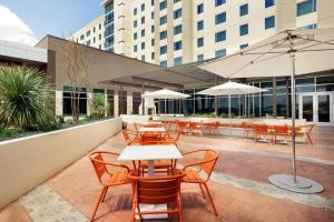 um pátio exterior com mesas, cadeiras e guarda-sóis em Embassy Suites By Hilton San Antonio Landmark em San Antonio