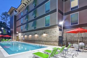 a pool in front of a building with chairs and an umbrella at Home2 Suites By Hilton Hilton Head in Hilton Head Island