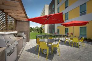 莱克兰Home2 Suites by Hilton Lakeland South Polk Parkway的一个带桌椅和红色遮阳伞的庭院