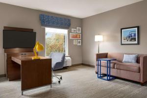 Habitación de hotel con sofá y escritorio con TV. en Hampton Inn & Suites Ocean City West, en Ocean City