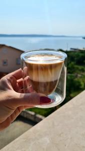 una mano sosteniendo un vaso de café frente al océano en Orkula Apartments, en Pašman