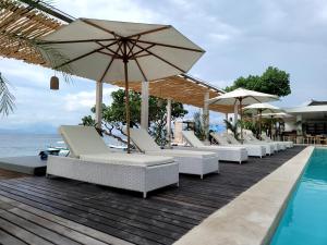 - une rangée de chaises et de parasols à côté de la piscine dans l'établissement AMP Beach House, à Nusa Penida