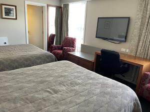 a hotel room with two beds and a desk and a television at Discovery Settlers Hotel in Whangarei