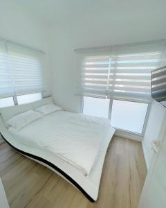 białe łóżko w pokoju z 2 oknami w obiekcie הבית בחוף הזהב w mieście Cezarea