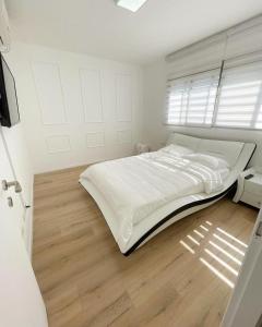 biała sypialnia z dużym łóżkiem i drewnianą podłogą w obiekcie הבית בחוף הזהב w mieście Cezarea