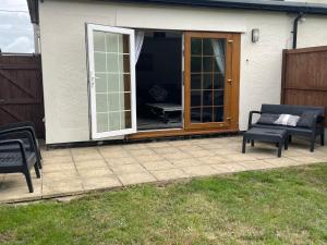 un patio con 2 sillas y una puerta corredera de cristal en Fern Cottage, en Thorpe le Soken