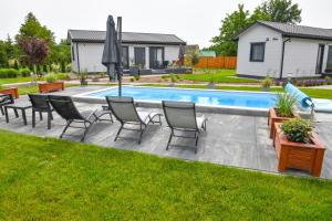 a pool with chairs and an umbrella in a yard at Barszczówka - domki, basen podgrzewany, prawdziwe jacuzzi, sauna infrared i inne atrakcje na Podlasiu in Kłyżówka