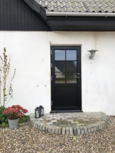 Una porta nera sul lato di una casa bianca di Gården på Bakken a Holme-Olstrup