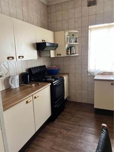 una pequeña cocina con estufa negra y armarios blancos. en Nomacurvy guest house, en Roodepoort