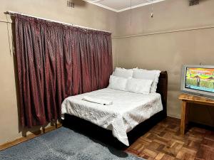 a small bedroom with a bed and a television at Nomacurvy guest house in Roodepoort
