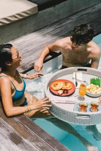 um homem e uma mulher sentados numa piscina com uma mesa de comida em Panorama Villas El Nido em El Nido